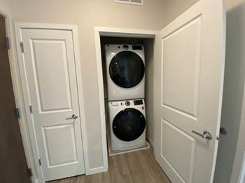 A white washing machine is in a small alcove between two doors.